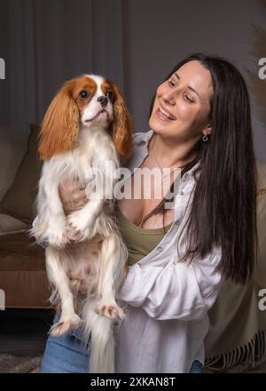 jeune femme rit joyeusement et joue avec son chien. Cavalier King Charles Cocker Spaniel Banque D'Images