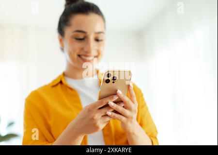 Utilisation du concept de gadgets. Photo d'une jeune femme positive assez arabe ou indienne défocalisée tenant un smartphone dans les mains, tapant un message dans les médias sociaux, naviguant sur Internet, vérifiant ses e-mails Banque D'Images