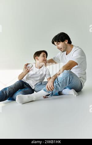 Un père et son fils sont assis ensemble sur un sol blanc, engagés dans une conversation. Banque D'Images