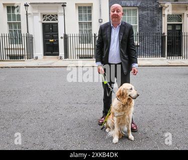 Londres, 22 juillet 2024. Steve Darling, député, avec son chien-guide Jennie. La National Federation of the Blind of the UK (NFBUK) remet une pétition au 10 Downing Street appelant à un arrêt temporaire de tous les arrêts de bus flottants prévus dans les nouvelles voies cyclables à travers le Royaume-Uni, car il s'agit d'une préoccupation importante pour la sécurité des personnes aveugles et autres. La pétition est organisée par Sarah Gayton (aux cheveux bleus), soutenue par le président de l'Association européenne des chiens aveugles, David Adams avec le chien Jimbo et le député de Libdem Steve Darling avec le chien guide Jennie, Sarah Leadbetter avec Nellie, et d'autres. Banque D'Images