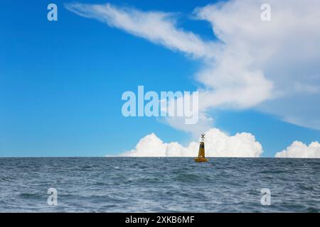 Bouée pilote jaune au milieu de la mer, le ciel avec des nuages blancs en arrière-plan. Banque D'Images