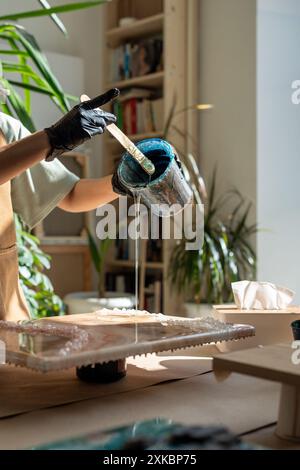 Mains de palmiers de l'artiste artisan dans des gants en latex créant des peintures époxy dans le studio ensoleillé d'art à la maison. Banque D'Images