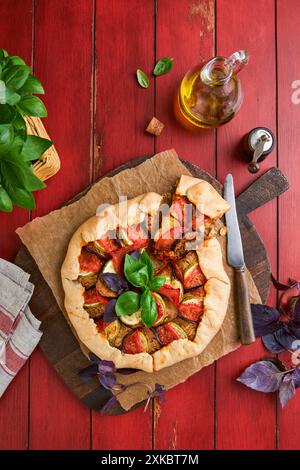 Galette ratatouille aux aubergines, courgettes, tomates. Plat traditionnel français fait maison avec des ingrédients et des ustensiles de cuisine sur la vieille table en bois rouge BA Banque D'Images