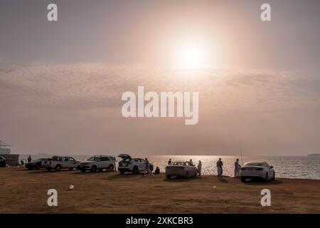 Des Arabes avec des voitures regardant le coucher du soleil sur la côte de la mer Rouge à Djeddah, Arabie Saoudite, sur la plage de la ville. Banque D'Images