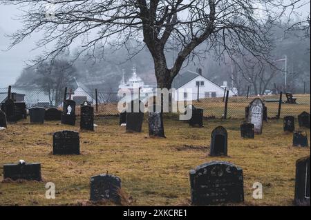 Cimetière sur Askøy (près de Bergen, Norvège) un jour de pluie en hiver. Il y a un bateau de pêche en arrière-plan. Banque D'Images