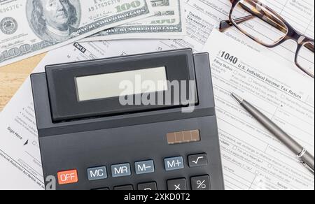 Calculatrice avec écran vierge, formulaires tex et billets de banque en dollars sur table. Vue de dessus Banque D'Images