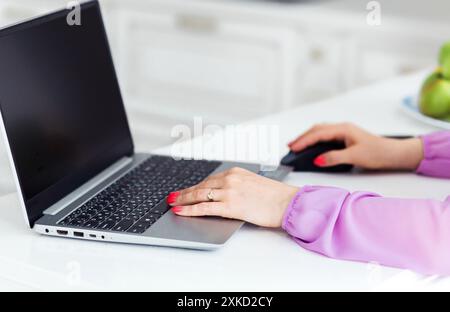 Une femme dans une blouse violette utilisant un ordinateur portable et une souris sur un bureau blanc. Banque D'Images