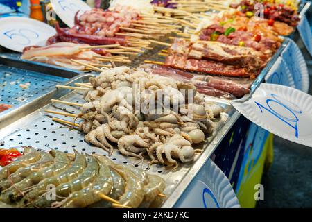 Assortiment de fruits de mer et brochettes de viande. Poulpes crues, crevettes et viande sur bâtonnets de bois. Cuisine thaïlandaise strret sur le marché nocturne. Cuisine asiatique Banque D'Images