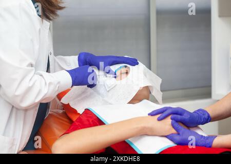 Procédé d'exérèse d'une lésion cutanée. Dermatologue réalisant une ablation d'une lésion cutanée bénigne sur le visage d'un jeune homme. Banque D'Images