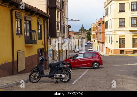 Astorga, Espagne - 3 juin 2023 : une voiture rouge est garée dans une rue étroite d'Astorga, Espagne. Un scooter noir est garé à proximité. Bâtiments jaune vif l Banque D'Images