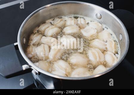 Boulettes pelmeni avec viande hachée remplissant bouillir dans le bouillon chaud dans une casserole en acier sur le poêle à la cuisine, progression de la cuisson, eau bouillonnante Banque D'Images