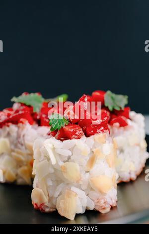 Un rouleau de sushi fusion moderne surmonté de fraises coupées en dés et garni de feuilles vertes sur fond sombre Banque D'Images