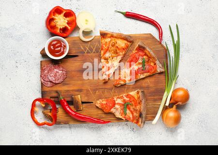 Planche en bois avec de délicieuses tranches de pizza, des ingrédients et un bol de sauce sur fond grunge blanc Banque D'Images