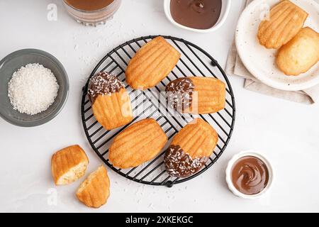 Grille de délicieuses madeleines, bols de crème au chocolat et flocons de noix de coco sur fond blanc Banque D'Images