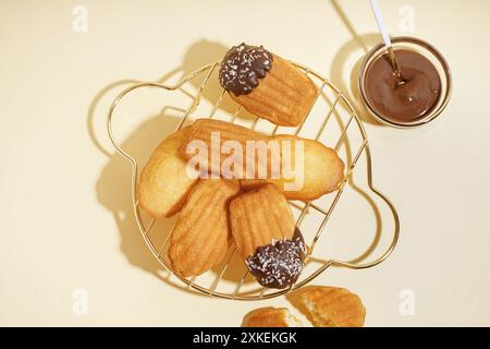 Grille avec de délicieuses madeleines et bol de pâte de chocolat sur fond beige Banque D'Images