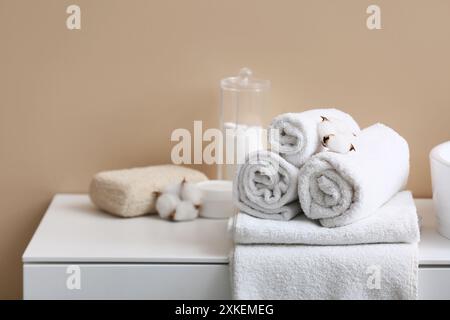 Propres serviettes douces, support avec des tampons de coton et des fleurs de coton sur la table près du mur beige dans la salle de bain, gros plan Banque D'Images