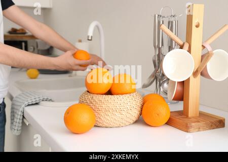 Les mains féminines se lavent à l'orange près du panier en osier avec des agrumes dans la cuisine blanche élégante Banque D'Images