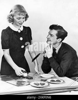 États-Unis mai 1942 Un jeune homme regarde adorablement une jeune femme alors qu'elle découpe des biscuits en forme de cœur. Banque D'Images