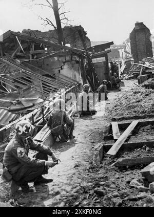 Ludwigshafen, Allemagne 4 avril 1945 les fantassins de la 94e division de la 3e armée américaine tiennent leurs canons prêts tout en couvrant un ami qui avance prudemment au coin d'un bâtiment détruit (fond) à Ludwigshafen pour une chasse aux tireurs d'élite. Banque D'Images