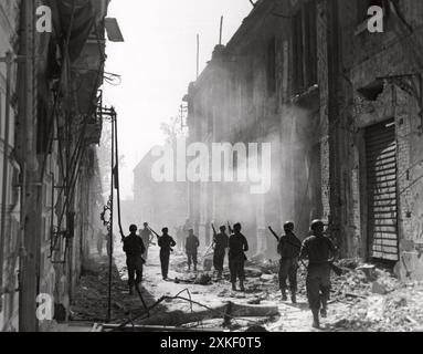 Messine, Italie août 1943 une unité de reconnaissance américaine marche à travers la fumée des bâtiments en feu tout en recherchant des tireurs d'élite ennemis juste après la capture de Messine par les troupes alliées. Banque D'Images