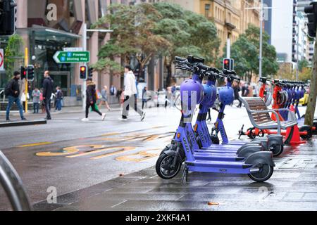 E-scooters avec casques sur le bord de la route sur St Georges Terrace avec piétons traversant en arrière-plan, Perth, Australie occidentale. Banque D'Images