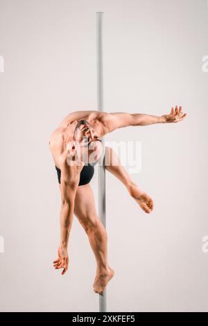 Musclé danseuse masculine à la perche fait la démonstration d'une pose difficile et artistique sur un perche Banque D'Images