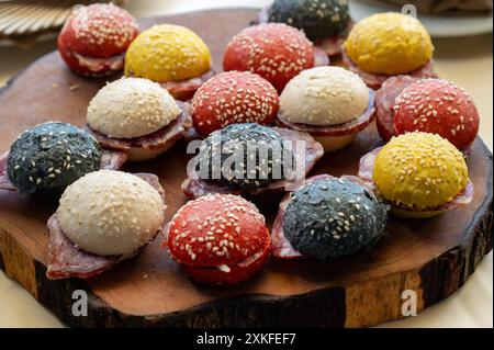 Savoureux petits sandwichs au salami avec des petits pains colorés présentés sur un plateau en bois rustique Banque D'Images