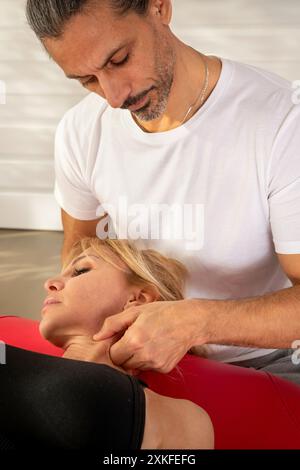 Ostéopathe effectue un massage du cou sur une femme allongée sur un lit rouge de physiothérapie Banque D'Images