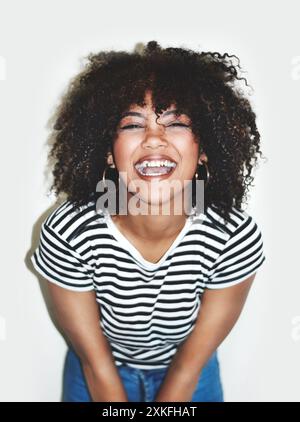 Afro, rire et portrait de femme en studio sur fond blanc pour comédie, humour ou blague. Émotion, drôle ou réaction et visage de personne heureuse Banque D'Images