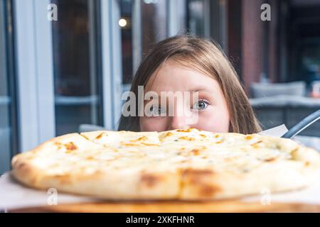 Jolie fille et pizza aux quatre fromages gros plan. Une jeune fille pré-adolescente regarde dans le cadre alors qu'elle se prépare à manger de la pizza. Foyer sélectionné. Photo de haute qualité Banque D'Images