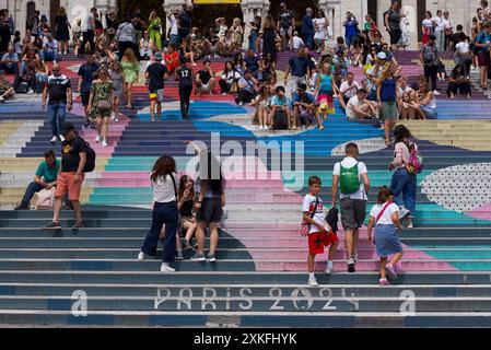 Paris, France, 07.22.2024. Des gens assis dans les escaliers à Montmartre. Les escaliers sont peints avec le logo olympique et le signe Paris 2024. Banque D'Images