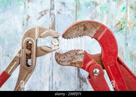 Deux clés réglables alimentant l'une l'autre un boulon sur le mur bleu défocalisé en stuc. Métaphore des bouches ouvertes affamées Banque D'Images