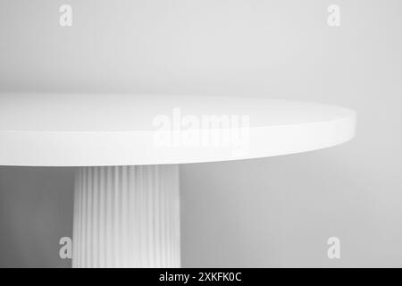 Dessus de table rond blanc avec pied de colonne, vue latérale sur fond de mur gris, toile de fond minimale pour la présentation ou l'affichage du produit, flou Banque D'Images