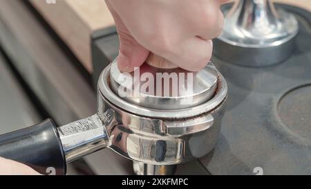 Gros plan d'un barista tassant du café moulu dans un porte-filtre pour préparer une dose d'espresso. Étape essentielle dans la préparation du café professionnel. Banque D'Images