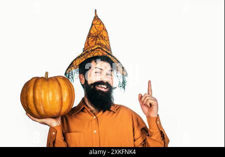 Bel homme dans le chapeau d'Halloween tenant la citrouille - portrait en gros plan. Bel homme d'Halloween avec citrouille à la main. Jeune homme avec chapeau de sorcière prêt à Banque D'Images