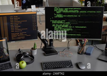 Photo de nature morte d'un bureau de travail de programmeur avec écouteurs et plusieurs ordinateurs affichant des lignes de code à l'écran dans le bureau Banque D'Images