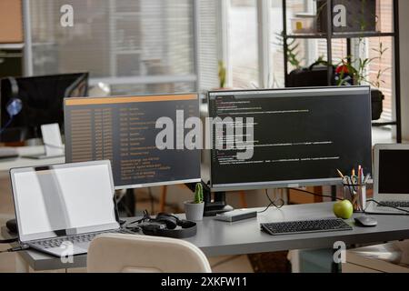 Plan d'arrière-plan de la configuration du pupitre de programmeur vide avec un ordinateur portable et plusieurs écrans d'ordinateur affichant la programmation du code source sur le lieu de travail du bureau Banque D'Images