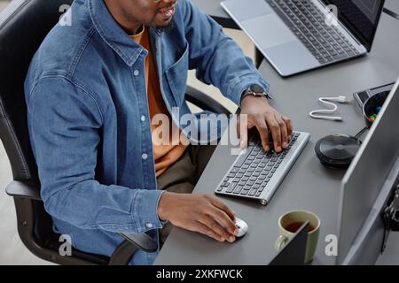 Photo recadrée à grand angle d'un employé afro-américain masculin dans une entreprise INFORMATIQUE tapant sur le clavier un code de programme en écrivant le code tout en étant assis à son bureau de travail dans le bureau Banque D'Images