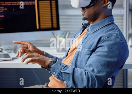 Vue latérale recadrée d'un ingénieur logiciel afro-américain masculin concentré codant dans un casque à l'aide de systèmes VR sur le lieu de travail de bureau, copyspace Banque D'Images