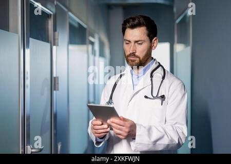 Docteur en manteau blanc utilisant la tablette numérique dans le couloir de l'hôpital. Professionnel médical vérifiant les dossiers des patients et les informations dans les soins de santé modernes fac Banque D'Images