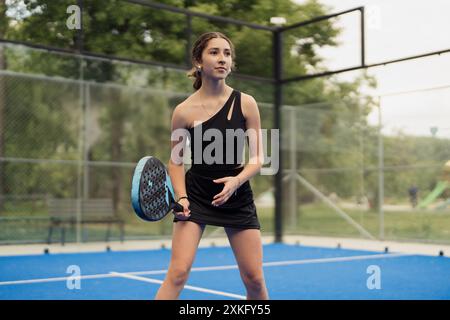 Femme jouant au padel tennis sur un court extérieur en tenue noire Banque D'Images