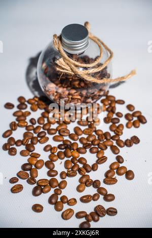 une collection de grains de café frais avec une couleur brun vif qui sont mis dans une bouteille en verre ronde fermée entourée d'une aspersion de grains de café Banque D'Images