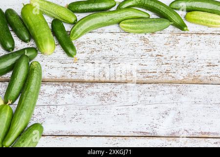 Une collection de concombres fraîchement récoltés disposés sur un fond en bois blanc altéré, mettant en valeur les produits naturels du jardinage et l'agriculture biologique. Banque D'Images