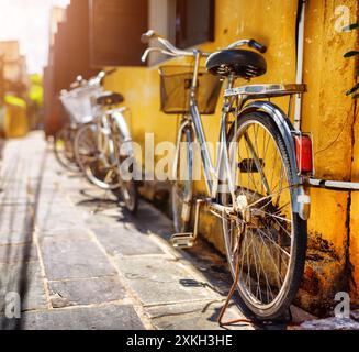 Vélos garés près du mur jaune sur la rue ensoleillée en été Banque D'Images