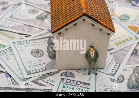 Figurine d'homme à côté de la maison sur fond de dollars Banque D'Images