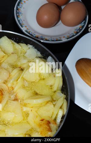 Faire une omelette espagnole, pomme de terre et oignon. Vous pouvez voir quelques œufs et une cuillère en bois avec laquelle il cuit Banque D'Images