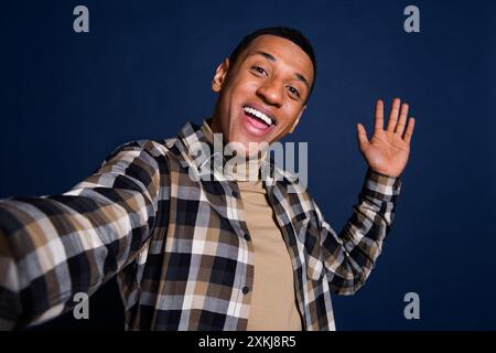 Portrait photo de jeune homme attrayant prendre selfie photo vague habillé à la main vêtements à carreaux élégants isolés sur fond de couleur bleu foncé Banque D'Images