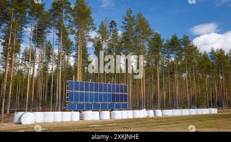 Panneaux solaires et balles d'alimentation du bétail enveloppées dans du plastique à la lisière de la forêt, Finlande Banque D'Images