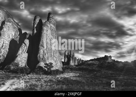 Arcs National Park, Utah ; image en noir et blanc avec ciel orageux, soleil couchant, rochers et sentier menant à l'Arche de Dune de sable dans le parc national d'Arches. Banque D'Images