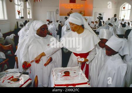 Moss Side, Manchester, Angleterre vers 1993. La Fraternité de la Croix et de l'étoile, les membres de l'église ont fait une sortie et une croisade de Londres à Manchester pour célébrer le 19e anniversaire de l'église en Grande-Bretagne. Un gâteau anniversaire avec l'image de OOO Olumba Olumba OBU sur le point d'être coupé et distribué parmi la congrégation. Cette église semi-chrétienne nigériane a été fondée par Olumba Olumba OBU, connu de ses disciples sous le nom de OOO. Ses membres l'adorent lui et Christ. Il croit qu'il est la huitième et dernière réincarnation de la Divinité. Banque D'Images